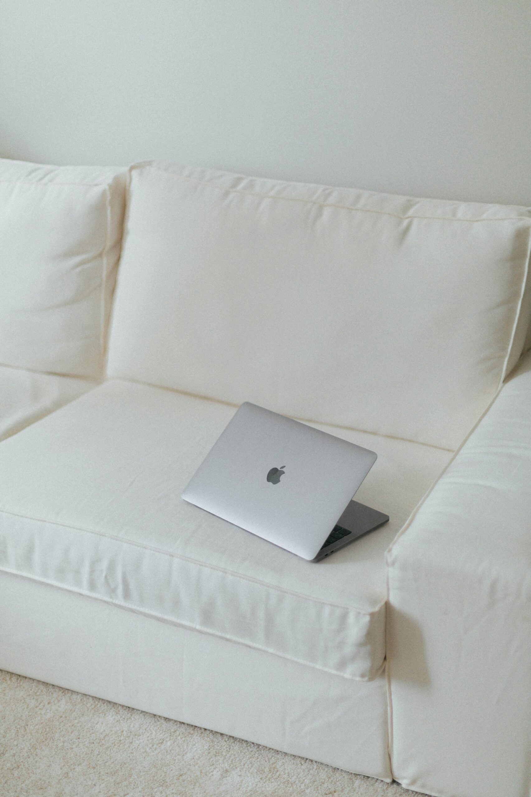 Sleek silver laptop on a clean white sofa in a minimalist setting, ideal for tech or modern lifestyle themes.